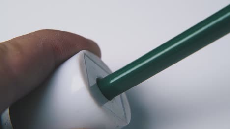 person puts green pencil into sharpener on light background