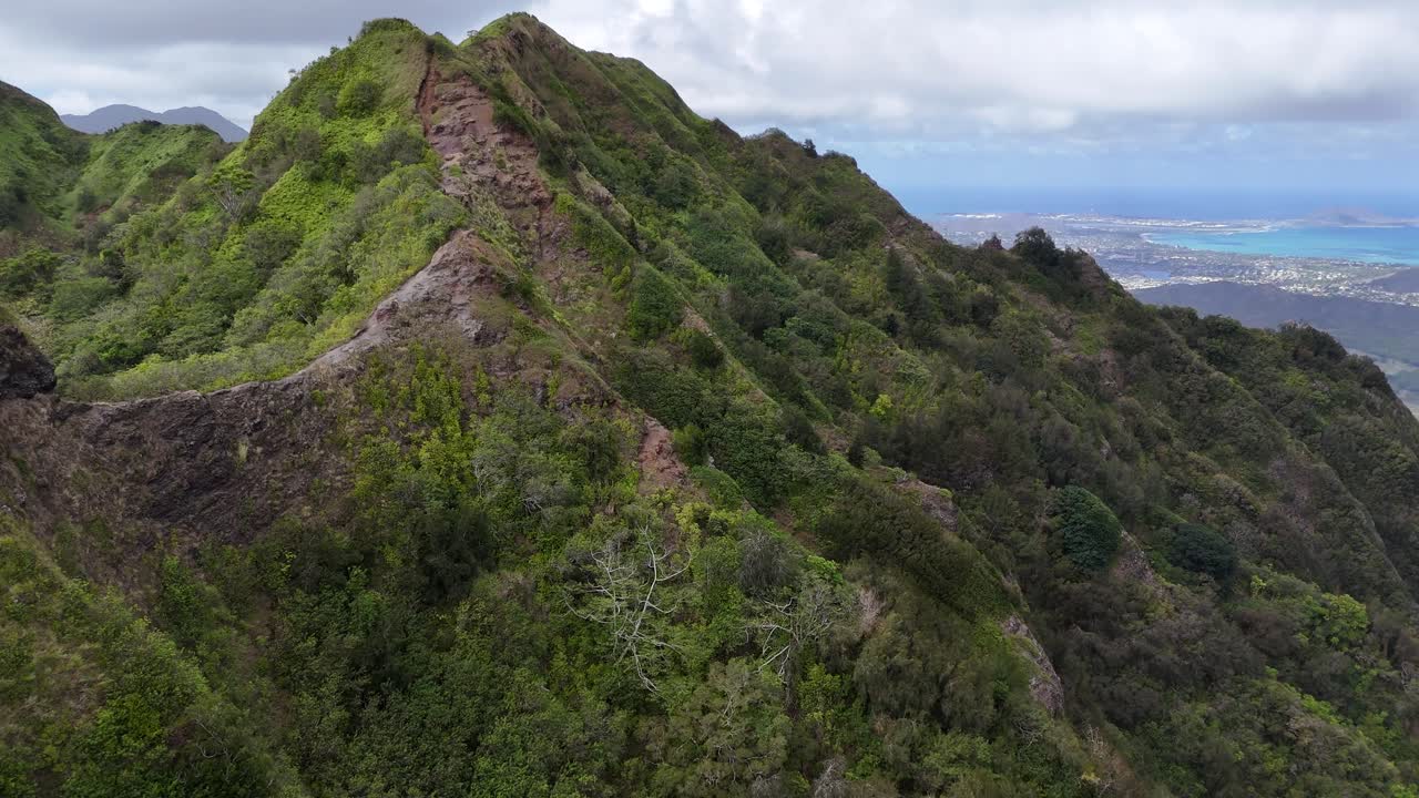 drone shot circling the rugged mountain ridge of Oahu, Hawaii, revealing dramatic cliffs, lush tropical scenery, and cinematic island atmosphere