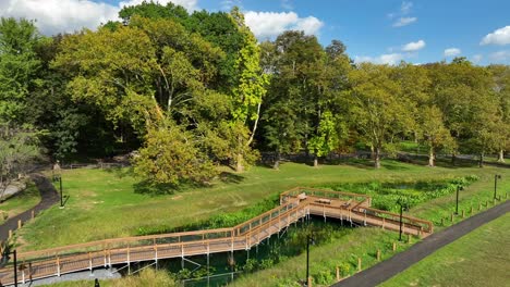 parque con un puente de madera, un sendero sinuoso y árboles exuberantes