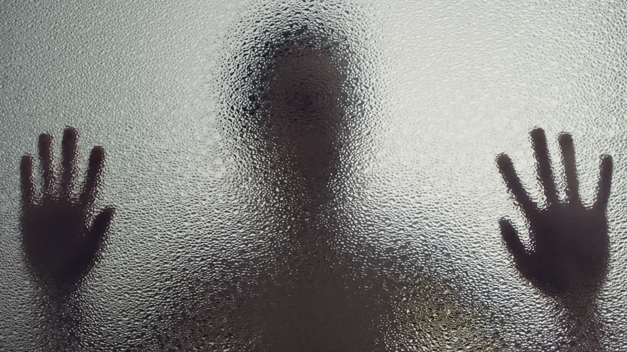 A female silhouette behind the frosted window touches the glass slowly