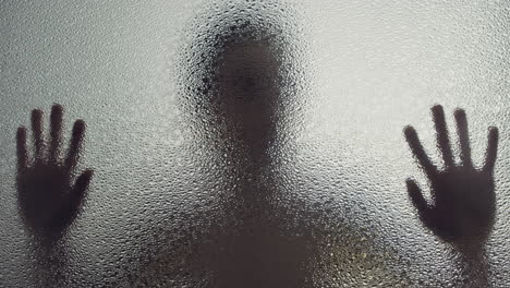 a female silhouette behind the frosted window touches the glass slowly