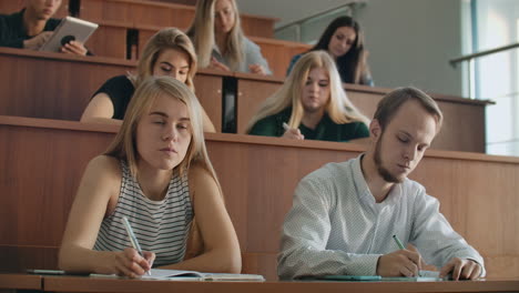 men and women students in ordinary clothes listen to a lecture in a large audience and write a lecture notes.