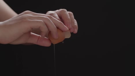 hands holding a cracked egg.breaking an egg.black background