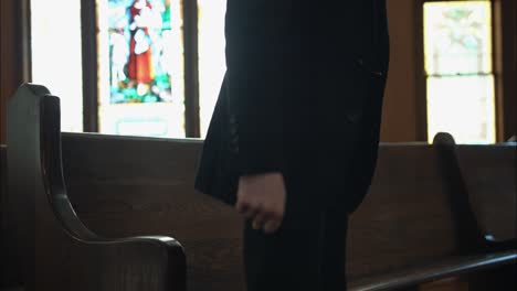 Pastor-in-black-suit-walking-in-church-sitting-in-pew-in-cinematic-slow-motion