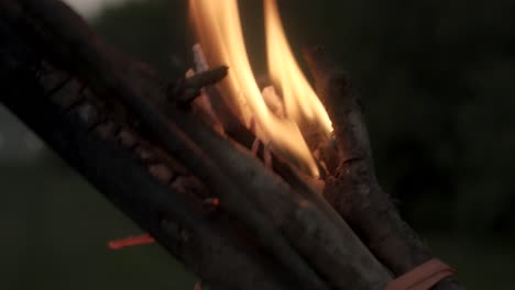A person’s hand twisting a burning torch made from sticks, with fire consuming one end