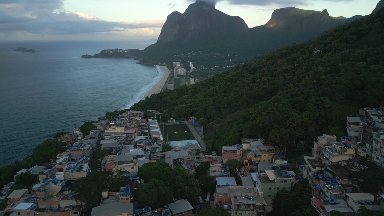 Casas de favela na encosta e o pico de granito da Pedra da Gávea durante o nascer do sol no início da manhã no Rio de Janeiro. Voo planado aéreo sobre as casas, filmado em 4K a 25 fps.