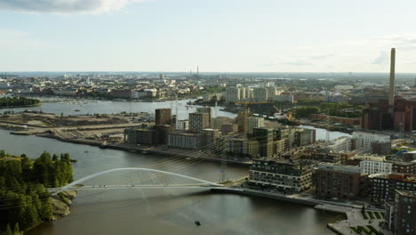 Aerial,-pan,-drone-shot-overlooking-a-bridge,-the-Kalasatama-and-Sompasaari-cityscape,-on-a-sunny-evening,-in-Helsinki,-Uusimaa,-Finland