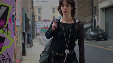 full length outdoor fashion portrait of young alternative style woman walking along london city uk street with graffiti covered walls in real time