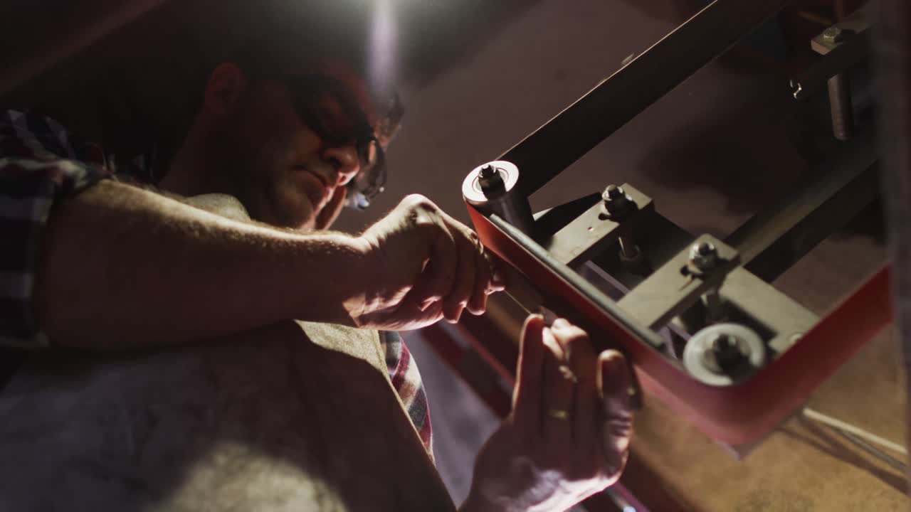 Primo piano di fabbricante di coltelli caucasico in officina che tiene un coltello e usa una levigatrice.