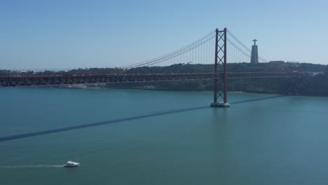 boat driving under the 25 of april bridge over the tagus river aerial drone reveal shot in lisbon, portugal liboa