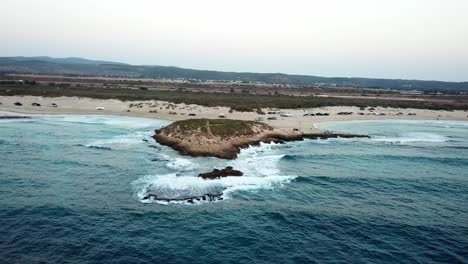 Secluded-coastline-of-sand-and-isolated-small-island-of-rock