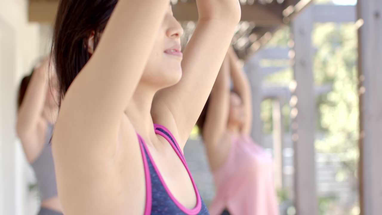 Practicing yoga outdoors, diverse women friends stretching and meditating in sunlight