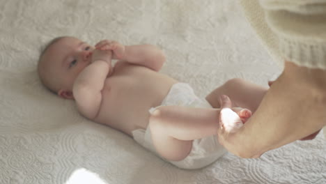 un bebé lindo y feliz acostado en la espalda, la madre jugando con las piernas pequeñas en sábanas blancas