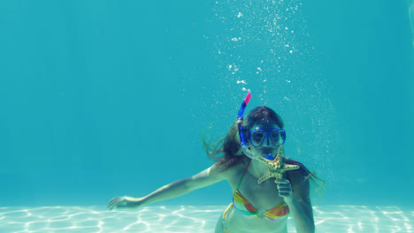 Happy-blonde-jumping-into-swimming-pool-wearing-snorkel-and-holding-starfish