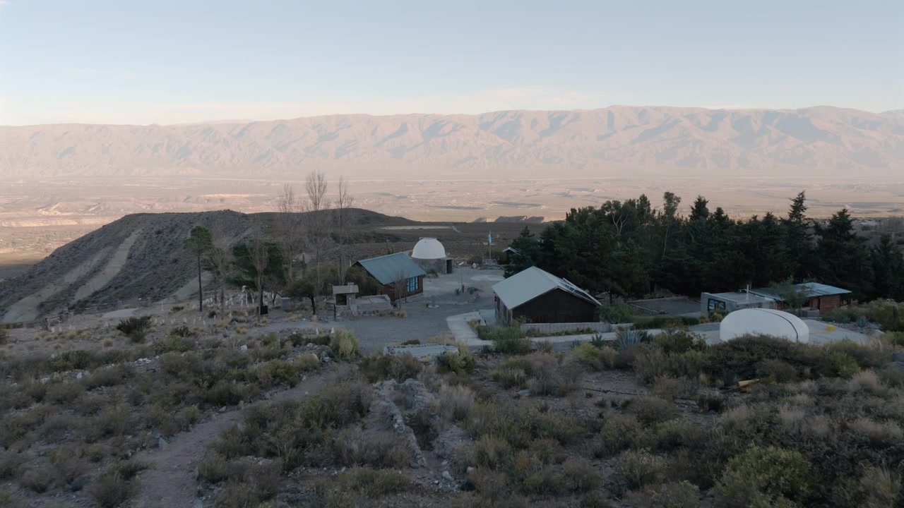 Drone passing above the Ampimpa Astronomical Observatory surrounded by mountain landscapes in Tafí del Valle, Argentina.