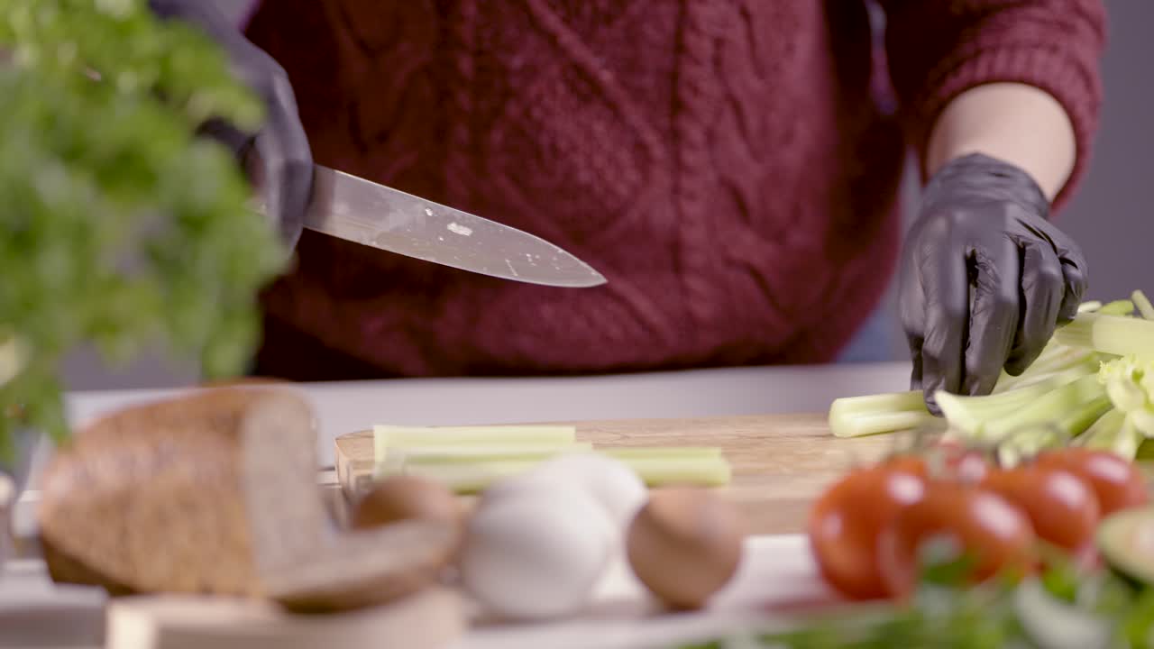 A chef carefully slices fresh leek on a wooden cutting board, wearing black gloves. The professional kitchen setting includes fresh ingredients, emphasizing precision, hygiene, and culinary expertise