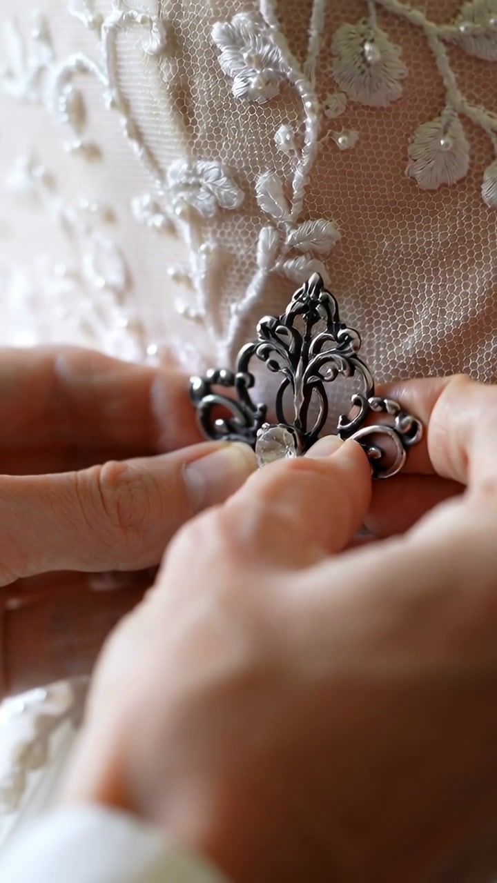 Hands cradling brooch, fastening onto gown while animated guides aligning brooch for bridal fit