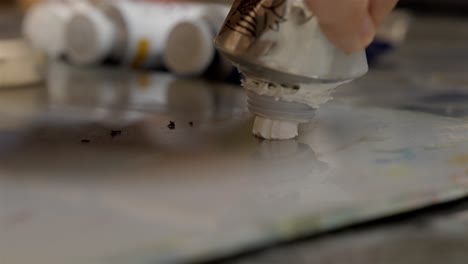 artists squeezes metallic tube of white oil paint onto mixing palette