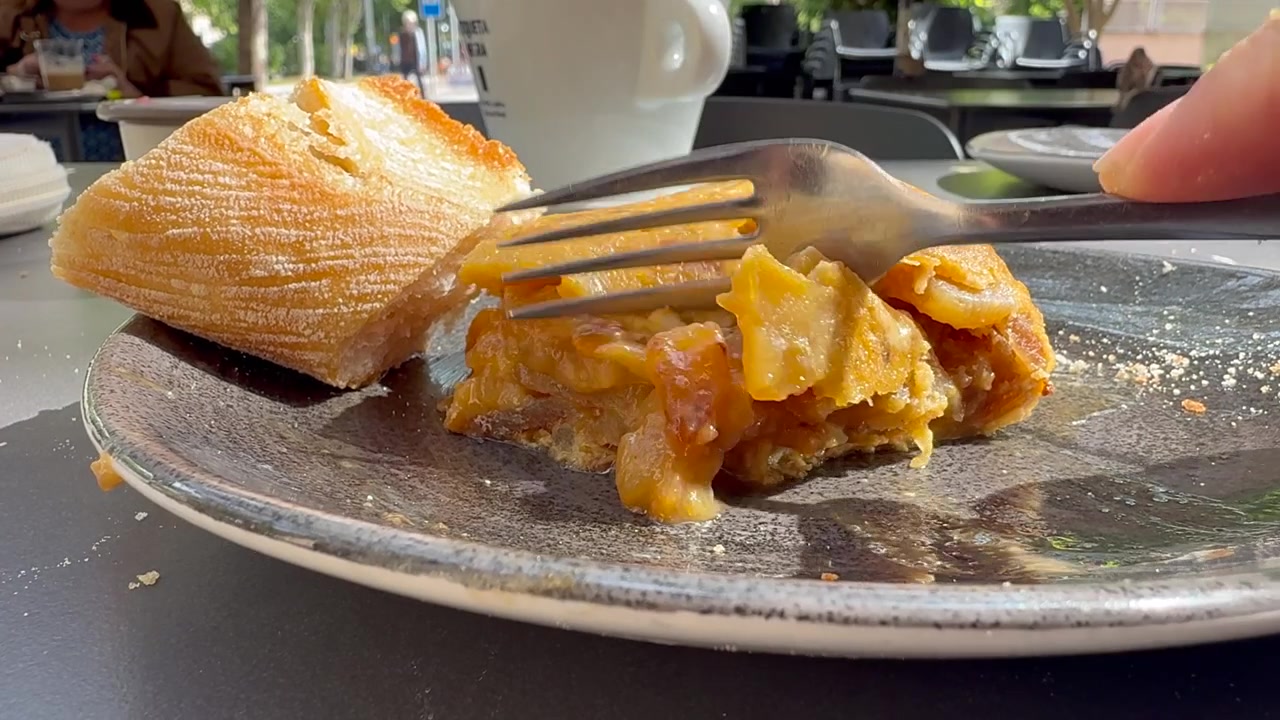 Vista ravvicinata della mano di un uomo caucasico che mangia una fetta di tortilla de patatas (frittata di patate spagnola) con una forchetta all'aperto su una terrazza.