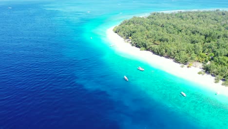 Beautiful-tropical-island-with-lush-vegetation-and-white-sandy-beach,-tourists-coming-by-boats-on-shore,-sailing-across-blue-turquoise-lagoon,-Indonesia