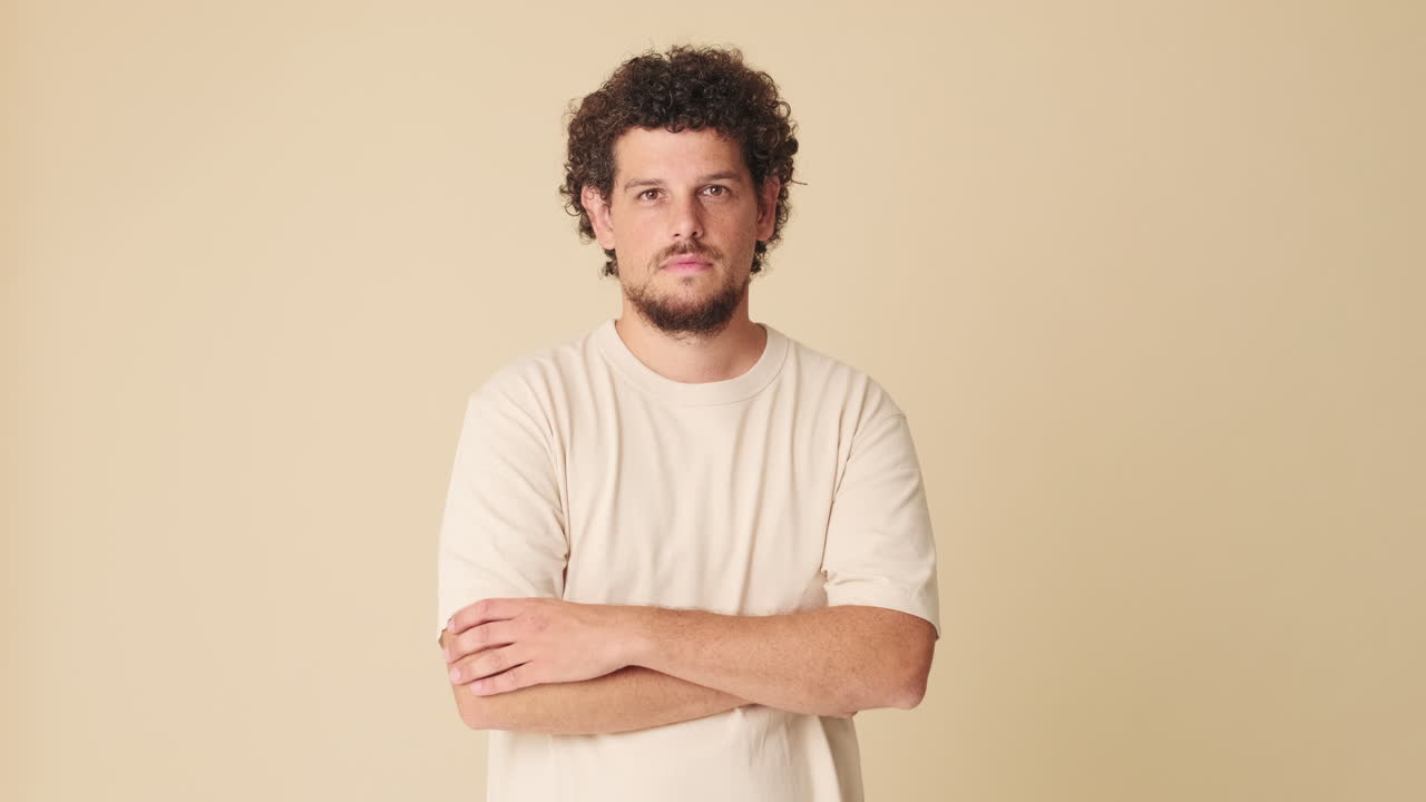 Confident Young Man with Curly Hair and Beard Posing with Arms Crossed
