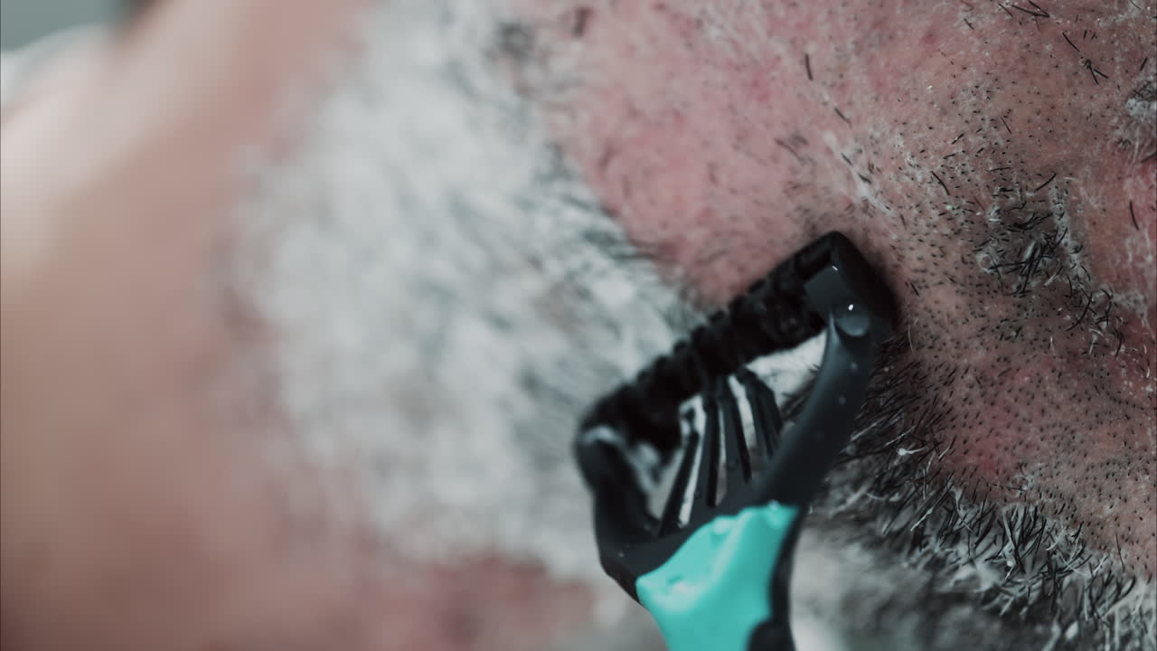 Close up of a man shaving his beard with a razor