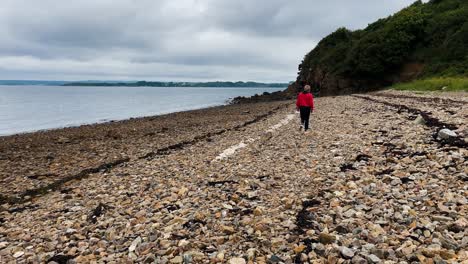 Woman-walking-down-toward-a-beach-in-front-of-rocks-in-France,-Brittany