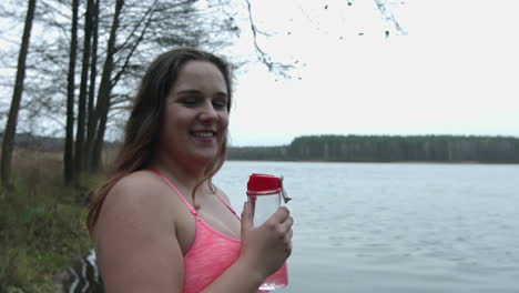 overweight woman drinking water from bidon after jogging in the park