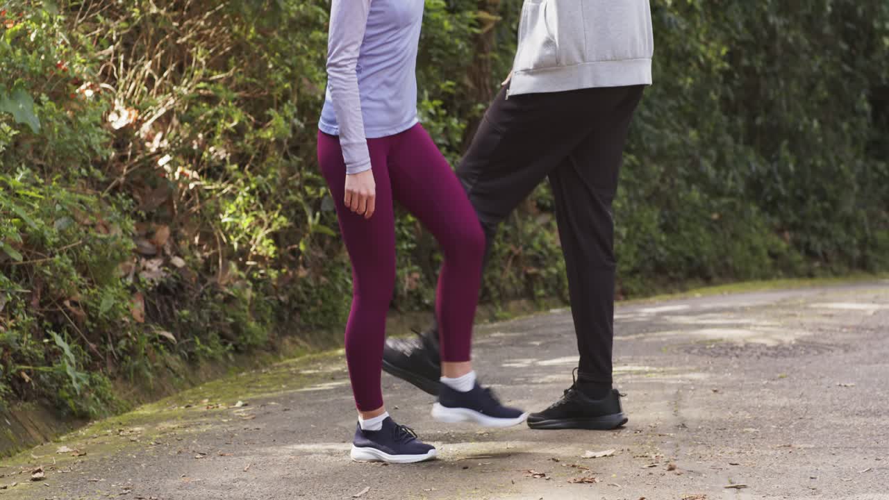 Compagni di allenamento in abbigliamento sportivo che sollevano le ginocchia e scalciano le gambe in sincronia su un sentiero lastricato per il fitness.
