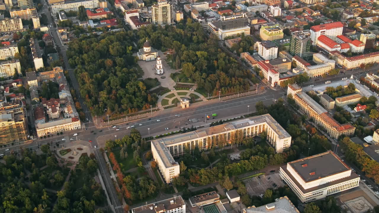 Aerial drone view of Chisinau downtown. Panorama view of multiple buildings, Government building and Central parks, roads with moving cars and lush trees. Sunset. Moldova