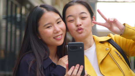 two smiling young female friends posing for selfie in urban setting together 3