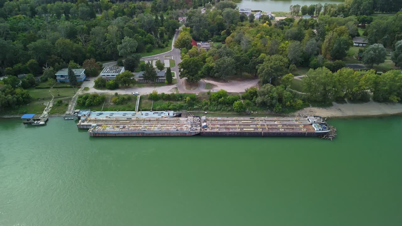 Aerial view of a harbor in Dunaújváros, Hungary, featuring docked barges and lush green surroundings