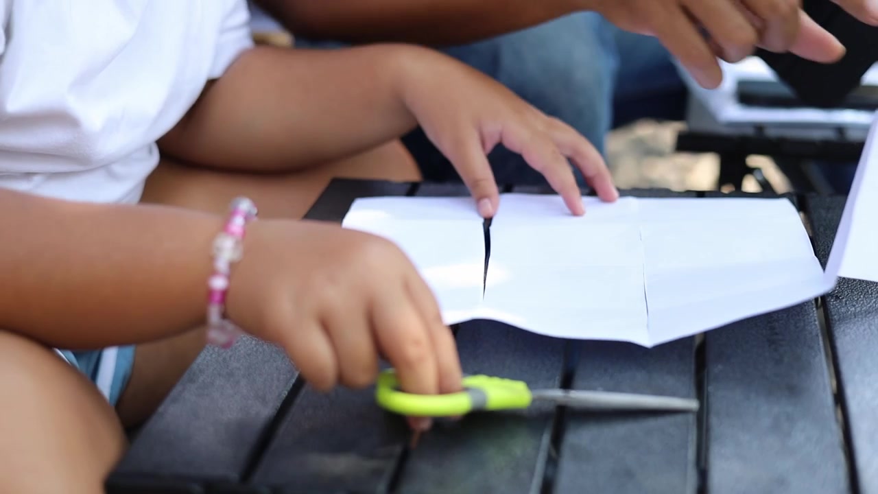 Young daughter learning paper crafting skills while her father guides and supports her during a creative activity at home. Close up