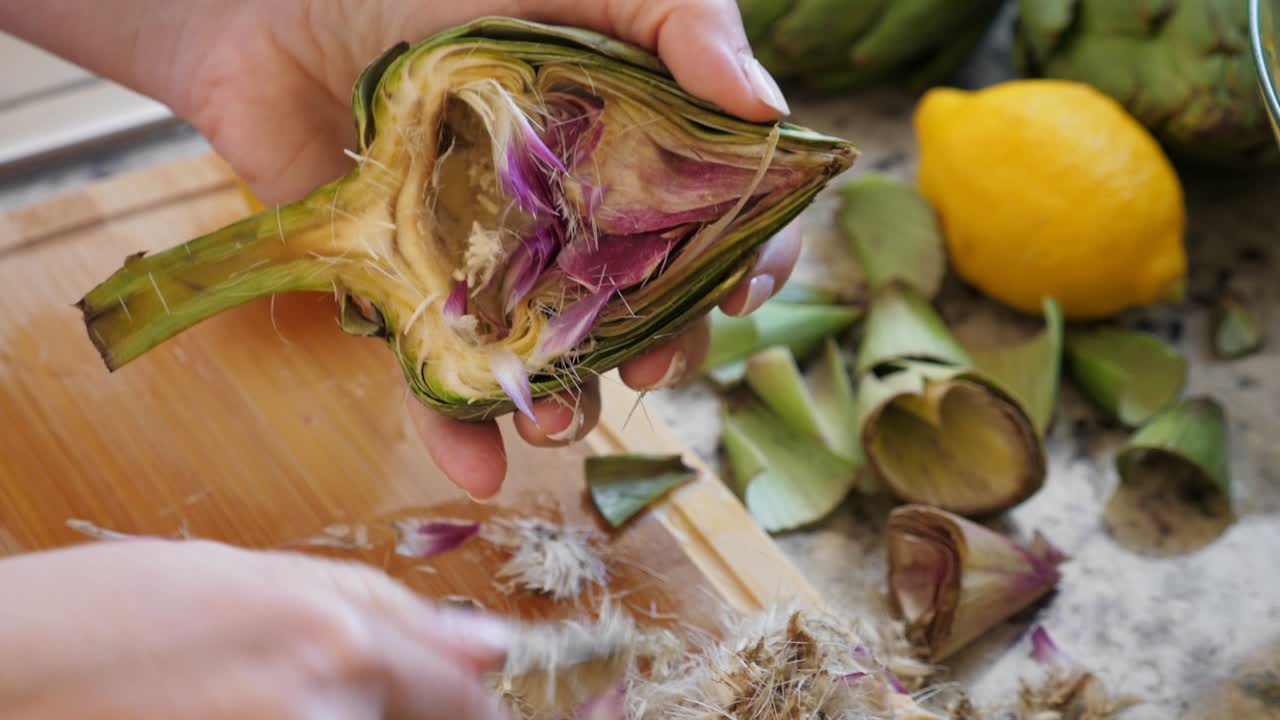 Woman cleaning heart of artichokes with spoon. Cooking process at the kitchen. Ready to prepare