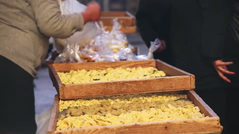 old women makes and sells traditional handmade orecchiette pasta, talking to the customers as she bags up their purchases, while pasta sits in racks to dry, no face, hands, static shot