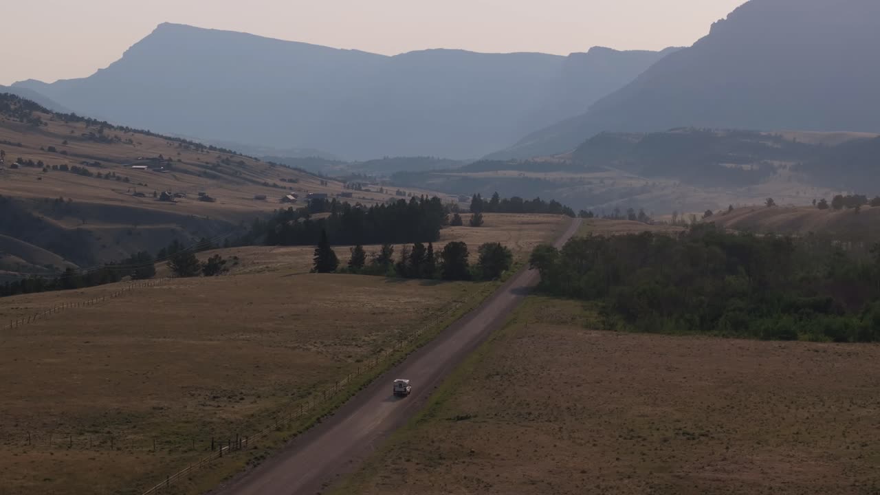 A van drives down a scenic road in Sunlight Basin with mountains in the background at dusk