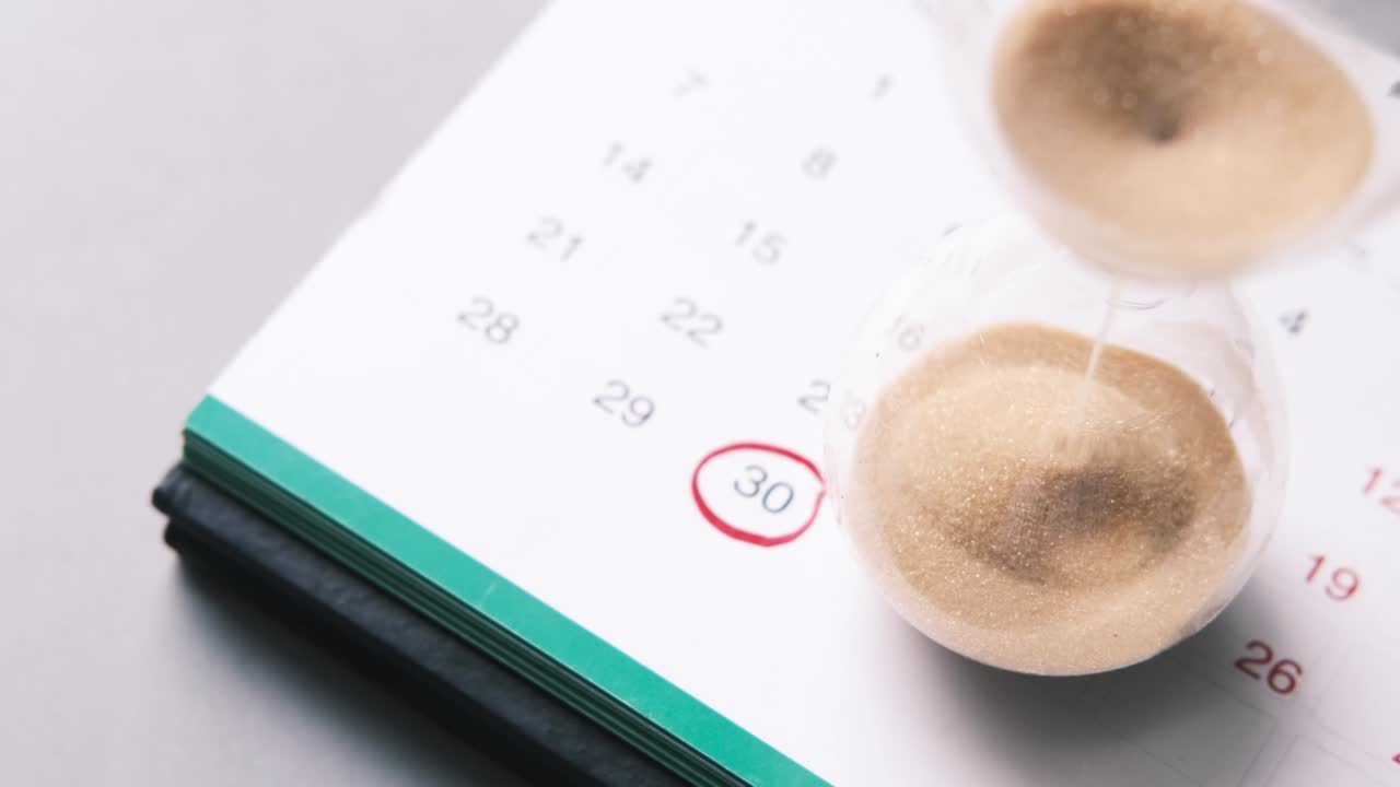 reloj de arena en un calendario, y fluyendo a través de la bombilla de vidrio de arena