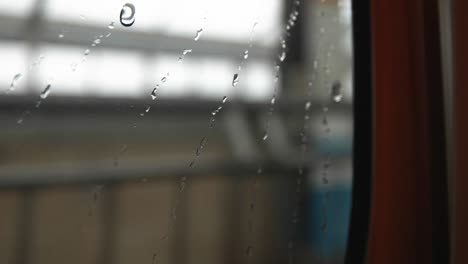 water dripping down on the window glass, blurry train station background, closeup