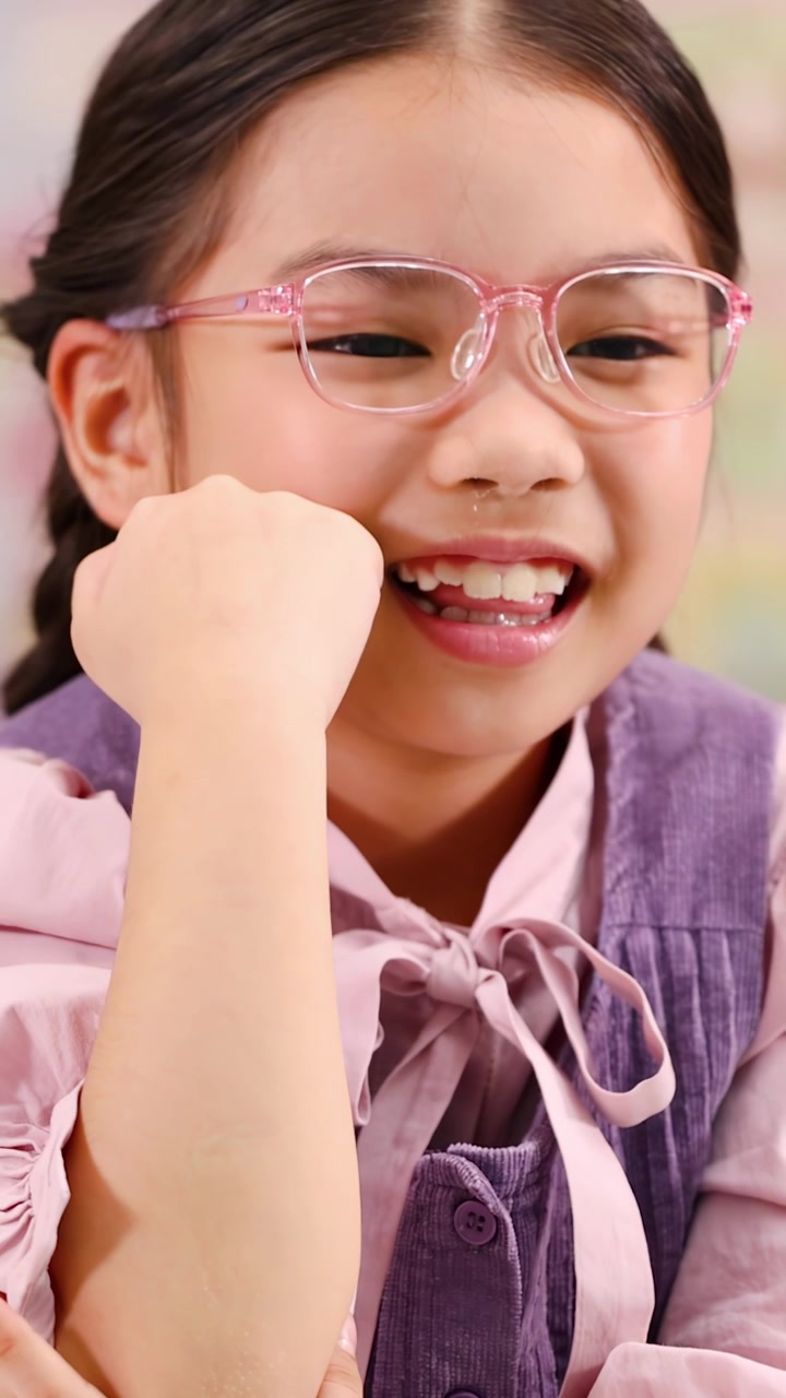 A joyful young girl in pink glasses smiles while flexing her arm in school