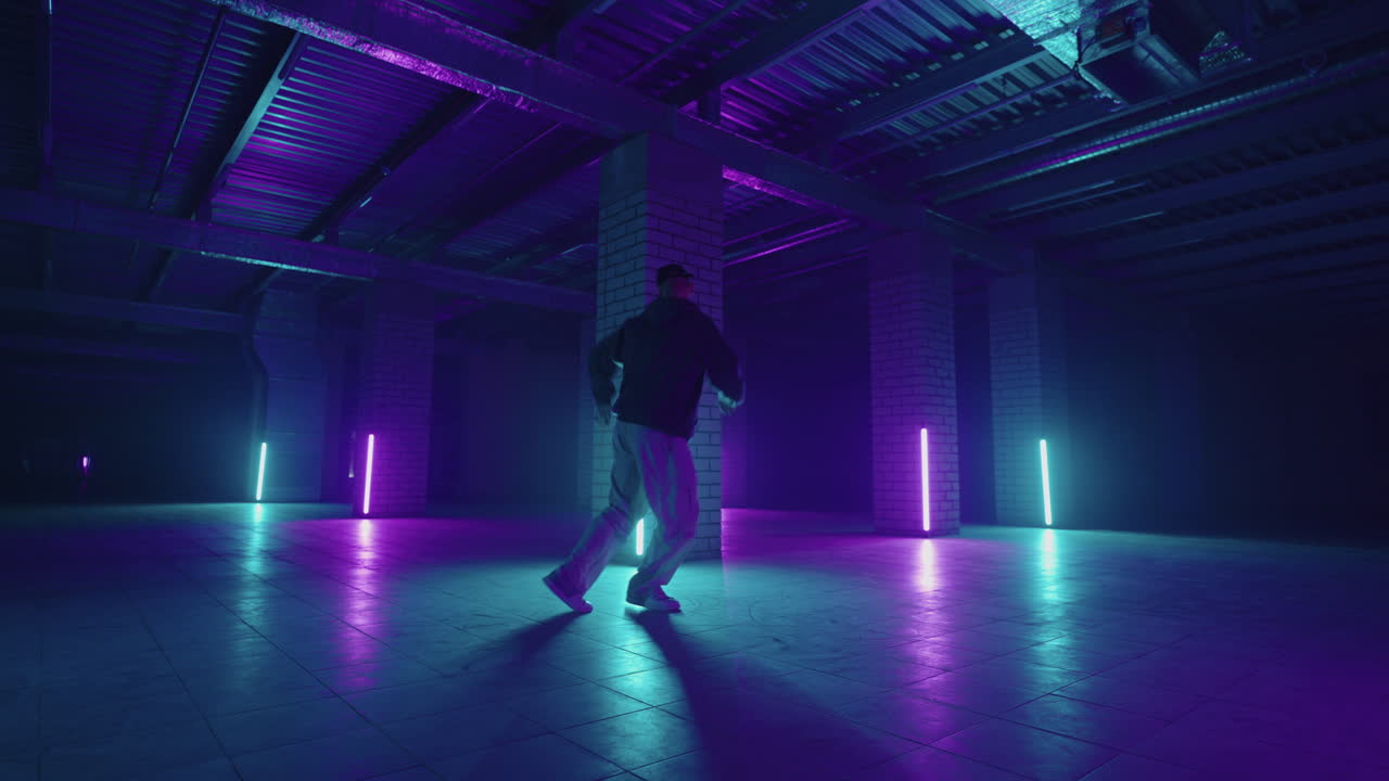 A steel man dances hip-hop freestyle in a modern style in a hall with neon light in purple blue colors. Male Professional Hip Hop Dancer
