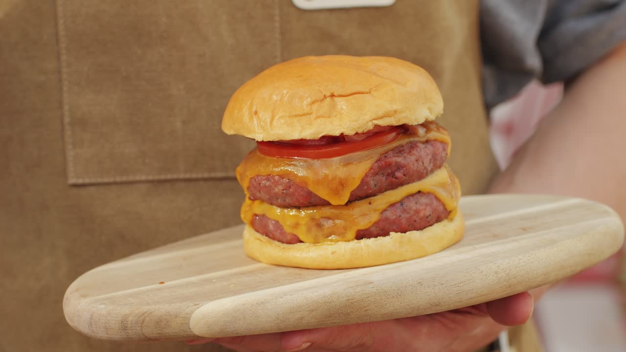 Making American fat smash burger with fresh tomatoes and cheese on grill close-up macro. Beef or pork cutlet smashing by burger press. The chef in kitchen of the restaurant making cutlets for burgers - smash burger beefsteak. Fast and street food concept.