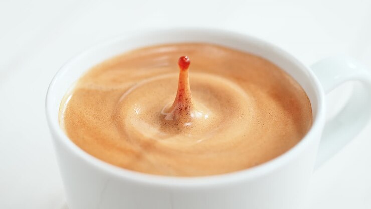 gotas de café cayendo y haciendo salpicaduras en una taza blanca con crema de café, fondo brillante