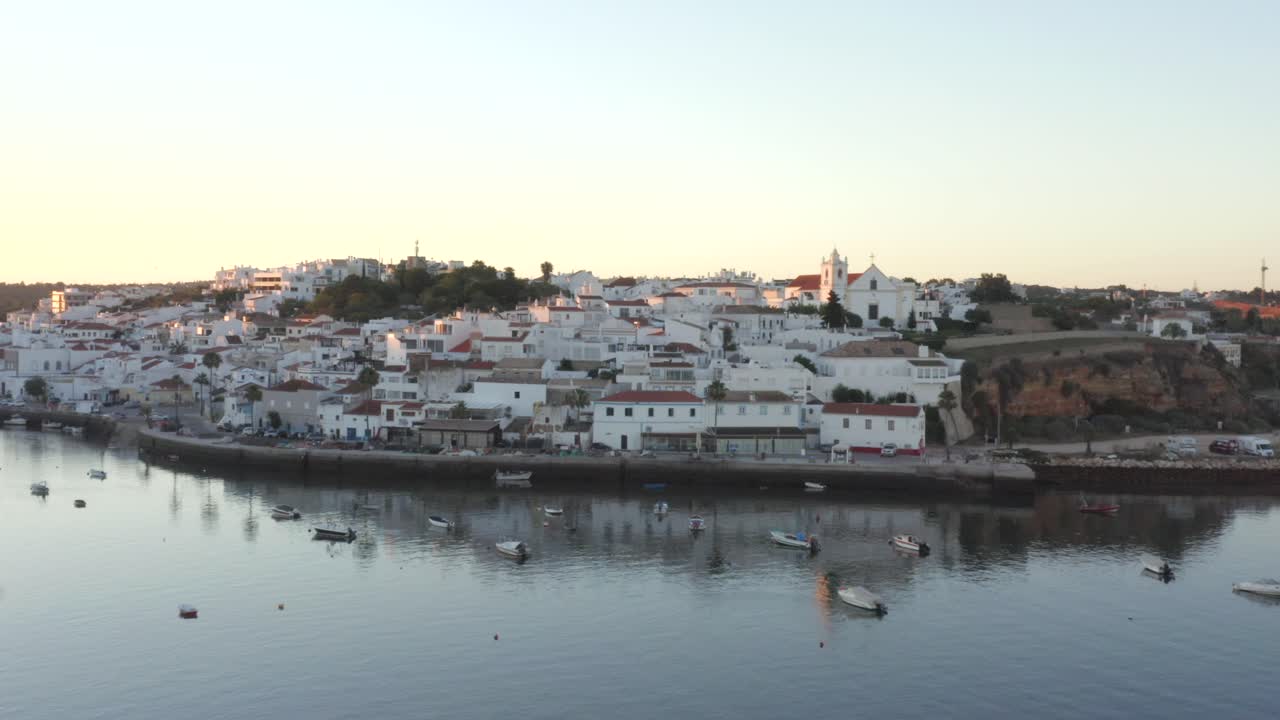 un río tranquilo que fluye frente a hermosas casas blancas mientras el sol arroja luz sobre los tejados en ferragudo, portugal