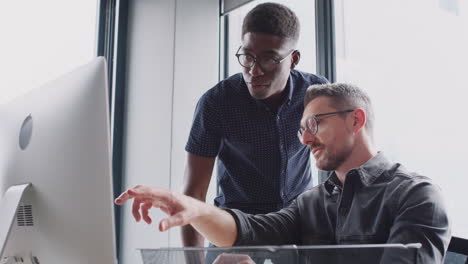 two male colleagues in discussion at a computer monitor in a creative office, low angle, close up