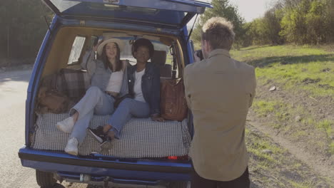 a young photographer taking pictures of to two beautiful young girls inside a caravan during a roadtrip