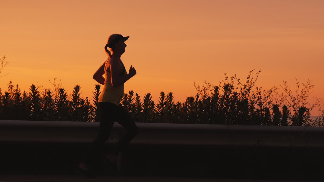 estilo de vida activo y saludable - silueta de mujer corriendo por la carretera a lo largo del mar al atardecer