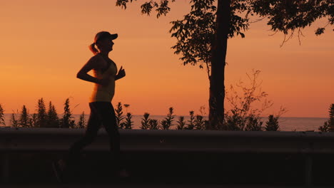 active and healthy lifestyle - woman silhouette running along the road along the sea at sunset