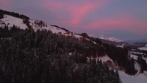 Aerial-shot-of-a-snow-covered-mountain-town,-winding-road-through-the-valley-during-sunset