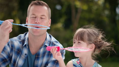 father and daughter blowing soap bubbles together in sunny park happy little girl having fun dad playing with child playfully enjoying summer 4k