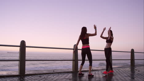 two athletic friends stretching before a run on promenade at sunset